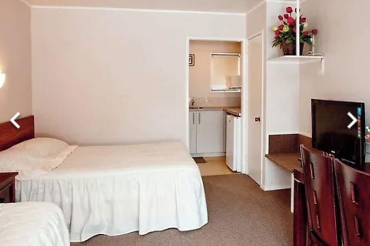 Un dormitorio con una cama individual, televisión y una pequeña kitchenette al fondo.