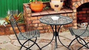 Een terras met twee metalen stoelen, een ronde tafel en een haard van baksteen.