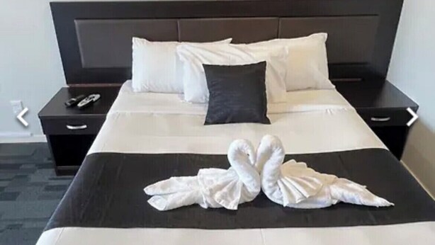 Een netjes opgemaakt bed met witte lakens en twee handdoeken gevouwen in de vorm van een hart.