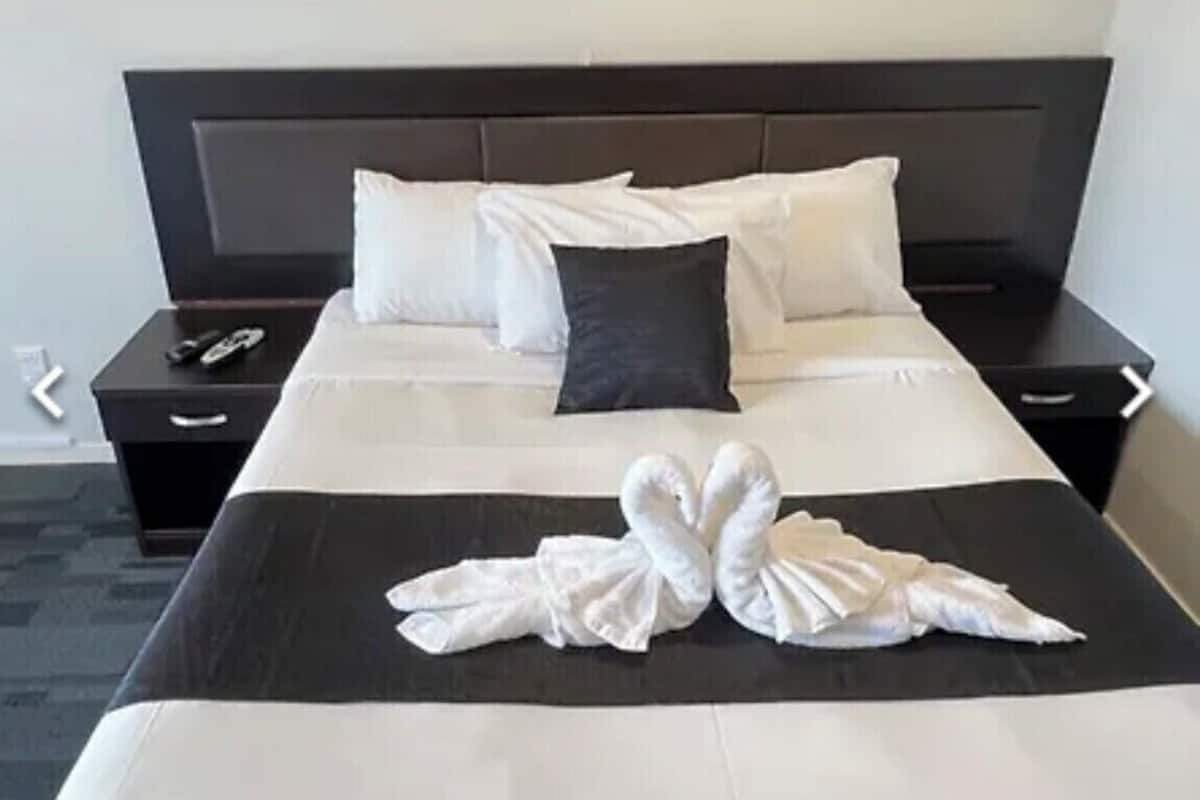 Una cama bien hecha con sábanas blancas y dos toallas dispuestas en forma de corazón sobre la cama.