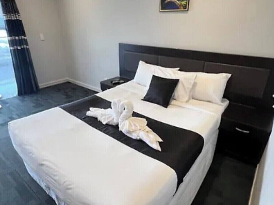A hotel room with a large bed, a nightstand, and a window with curtains.