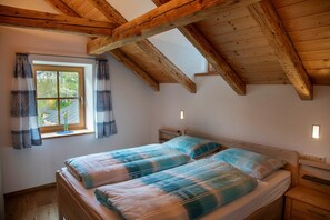 A bedroom with a sloped ceiling, a window with curtains, a bed with a blue and white checkered bedspread, and a bedside table. - Apartment 'Mulino Glurns' with Mountain View, Private Terrace and Shared Garden (Glorenza)