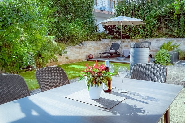 Une terrasse extérieure avec une table, des chaises, un pot de fleurs, une bouteille et un verre.