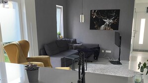 A modern kitchen with a sink, a dining area with a table and chairs, a sofa, and a large window.