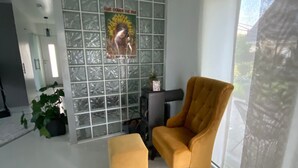 A modern living room with a large window, a yellow armchair, a small ottoman, and a decorative wall piece.