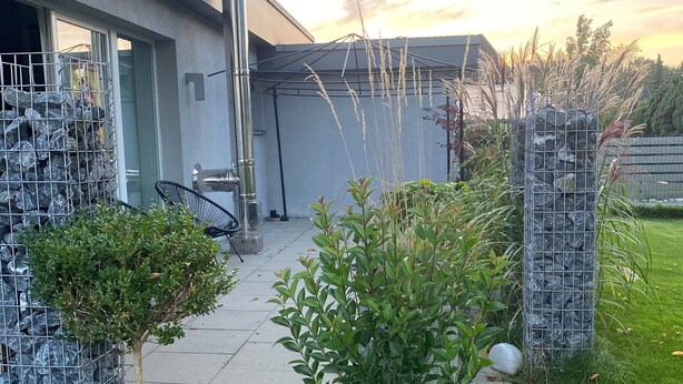 A modern building with a covered patio, a metal fence, and a small tree.
