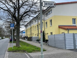 Une vue de rue avec un panneau de signalisation indiquant un espace de stationnement, un arbre et un bâtiment jaune doté d’une zone délimitée par une grille.