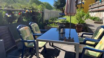 An outdoor patio with a table and chairs, surrounded by a wooden fence and greenery.