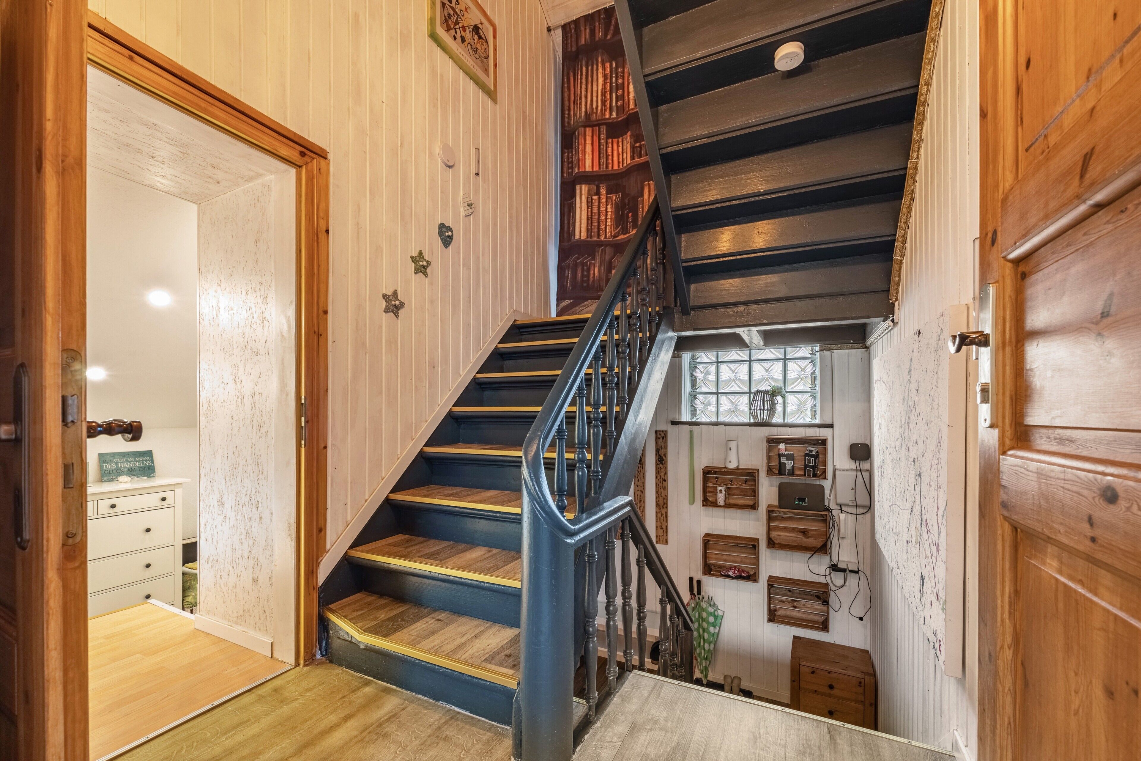 Una escalera de madera con barandilla azul que lleva a un rellano con un aparador blanco y una mesita.