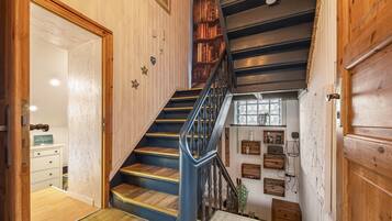 Una escalera de madera con barandilla azul que lleva a un rellano con un aparador blanco y una mesita.