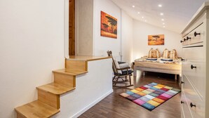 Un escalier menant à une chambre à coucher où se trouvent un lit, un fauteuil à bascule et un tapis aux couleurs vives.