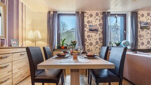 Un espace repas avec une table en bois, des chaises noires et une vue sur l’extérieur grâce à de grandes fenêtres.