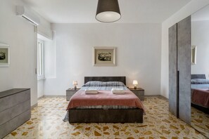 Een slaapkamer met een bed, nachtkastjes, een spiegel en een lijst met een afbeelding aan de muur.