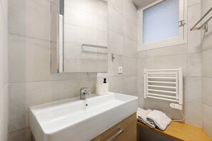 Une salle de bain avec un lavabo blanc, un miroir, un porte-serviettes et une fenêtre avec un vitrage dépoli.