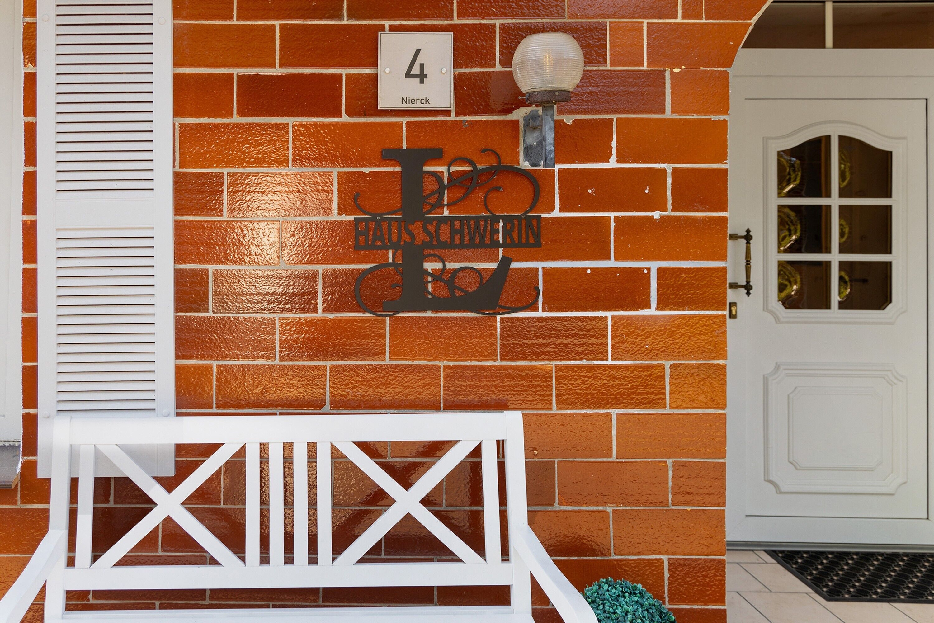 A brick wall with a metal sign, a white door with glass panels, and a white bench.