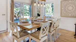 Un espace repas avec une table en bois, des chaises blanches et un luminaire suspendu.