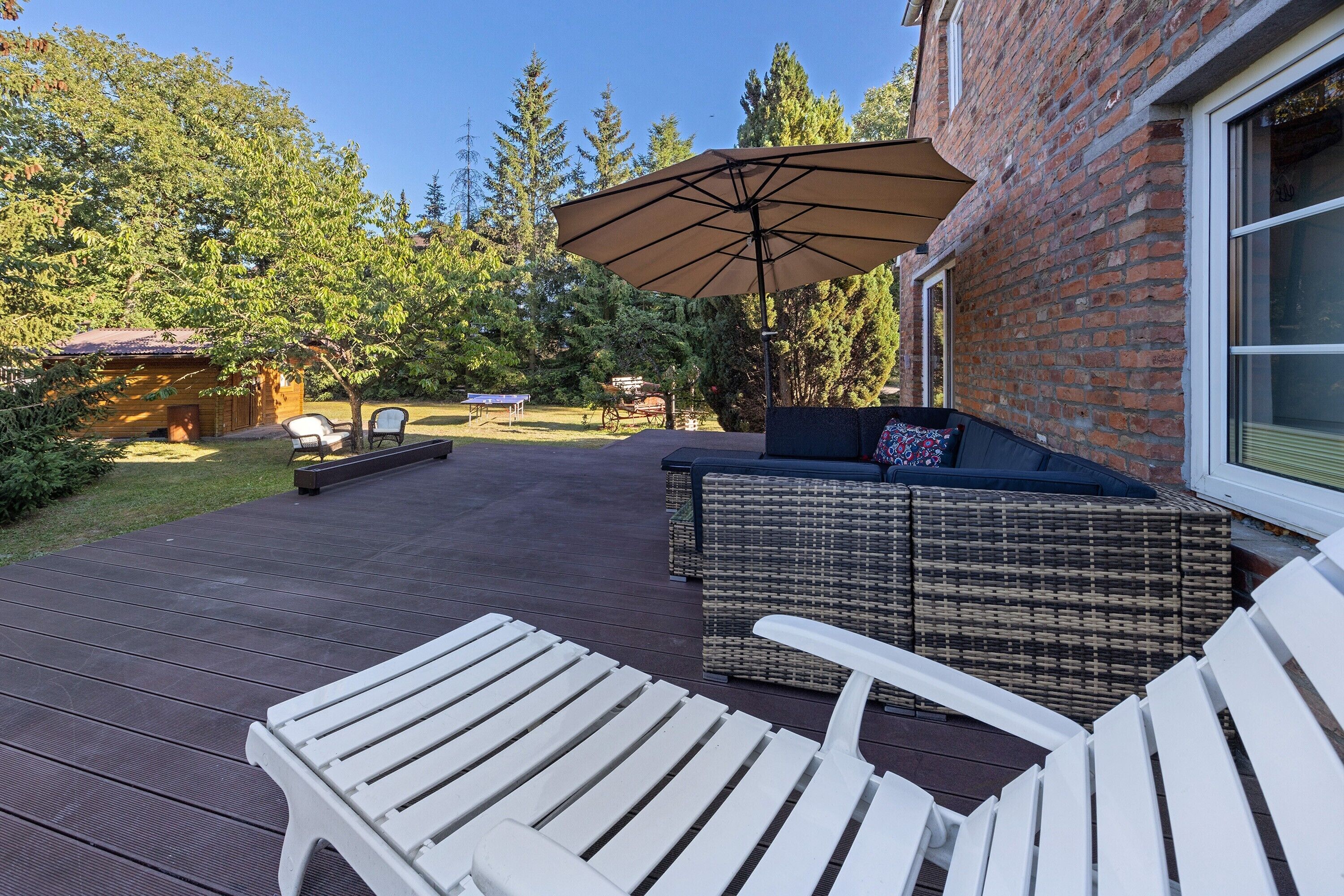 Une terrasse avec des chaises blanches, un canapé en osier et un grand parasol.
