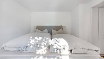 A bed with a grey headboard, white bedding, and a door to the right.