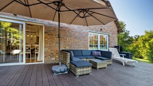 Une terrasse extérieure avec des meubles en osier, un grand parasol et un mur en briques.