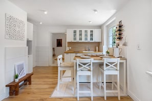 A modern kitchen with white cabinets, a wooden countertop, and a dining area with white chairs.