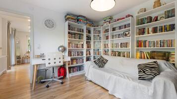Una habitación con un sofá blanco, una estantería llena de libros, un escritorio con una silla y un reloj en la pared.