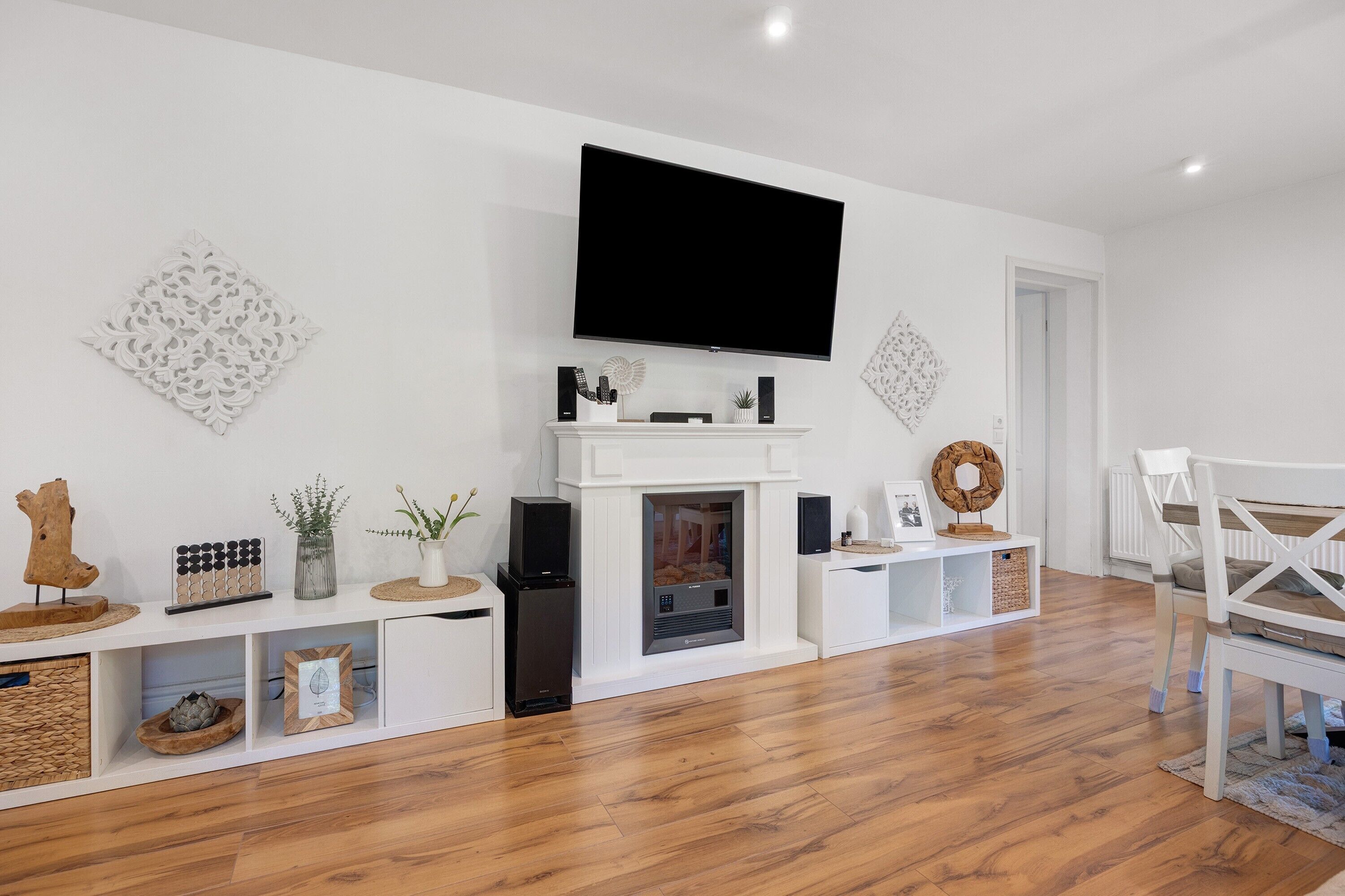 Una sala de estar moderna con televisor de pantalla plana, chimenea blanca y piso de madera.