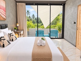 Habitación de hotel con cama, escritorio, silla y vista a zonas verdes a través de una puerta corrediza.