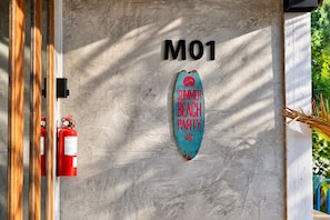 Un mur sur lequel on peut lire l’inscription « M01 » et un panneau en forme de planche de surf sur lequel est écrit « FÊTE D’ÉTÉ SUR LA PLAGE ».