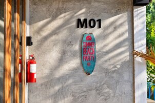 Una pared con un letrero que dice 'M01' y un letrero con forma de tabla de surf que indica 'FIESTA DE VERANO EN LA PLAYA'.
