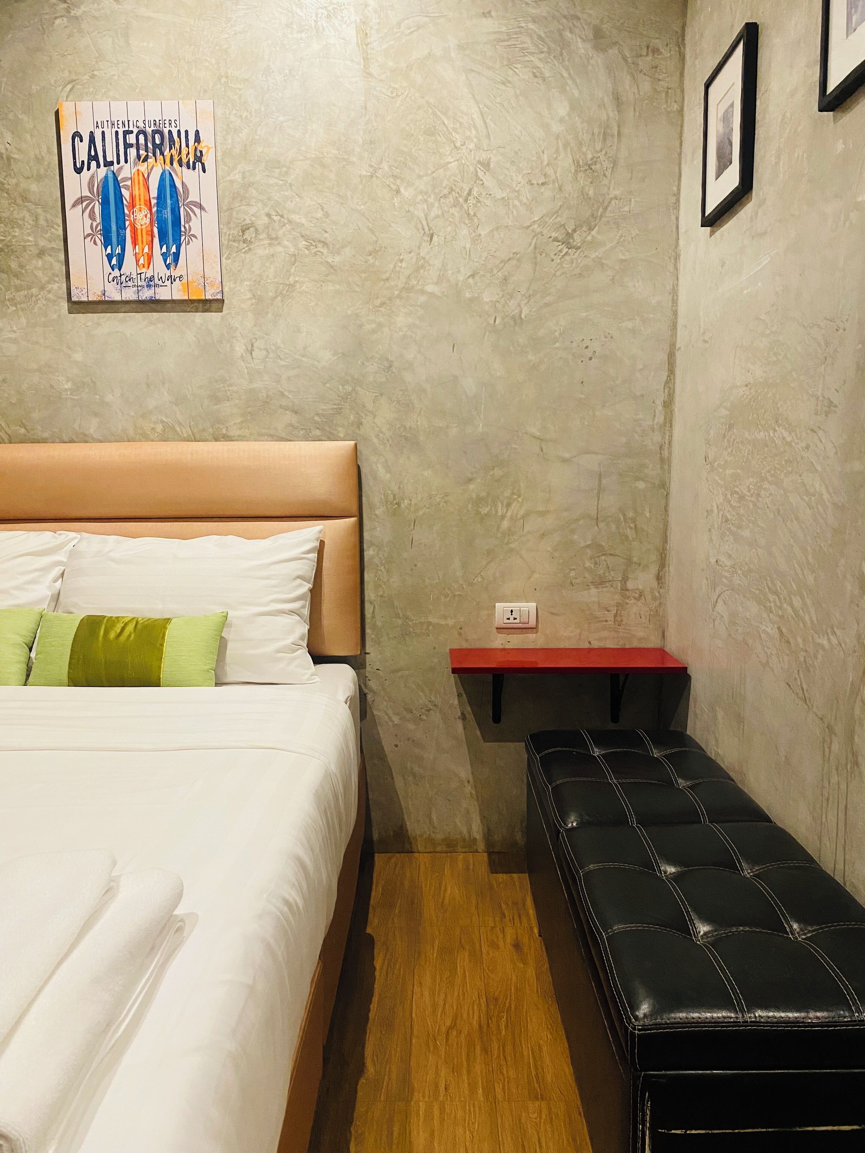 Ein Hotelzimmer mit einem Bett, einer Bank, einem kleinen Tisch und einer Wand mit einem Surfbrettposter.