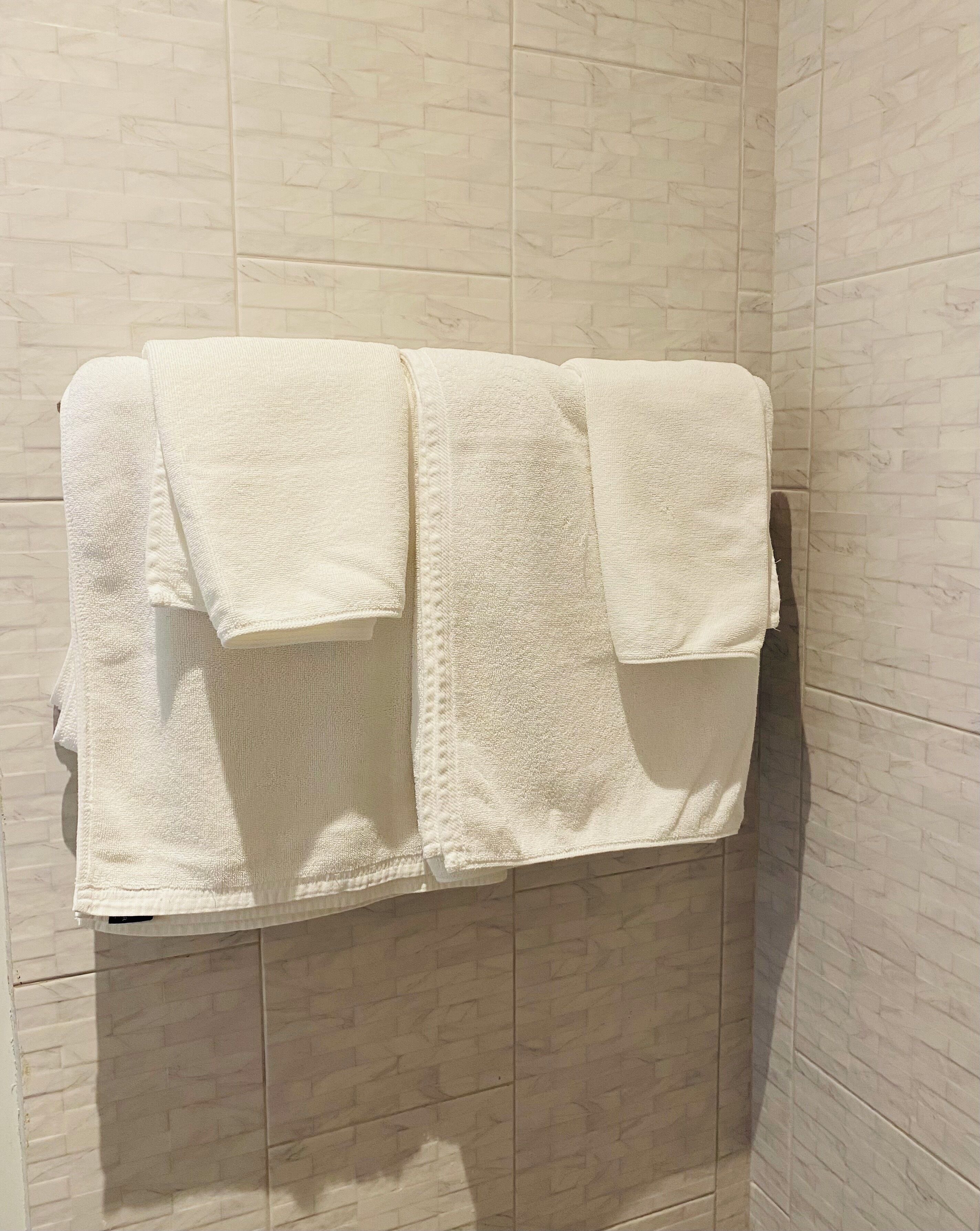 A bathroom with a towel rack holding three white towels. The walls are tiled with a marble pattern.