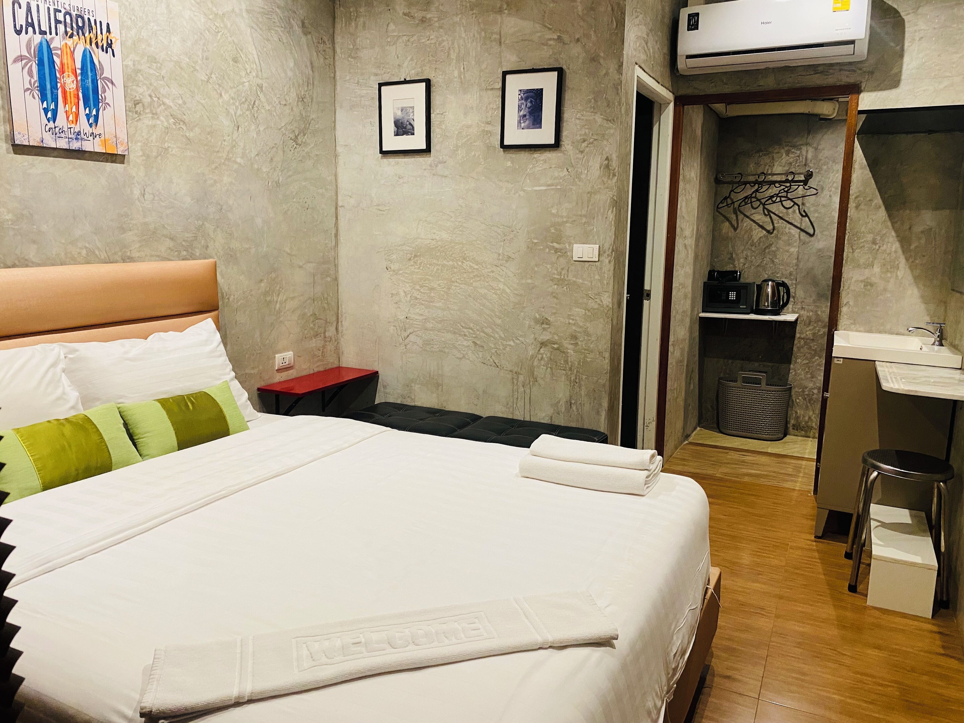 A hotel room with a bed, a desk, a chair, a small table, and a wall-mounted air conditioner.