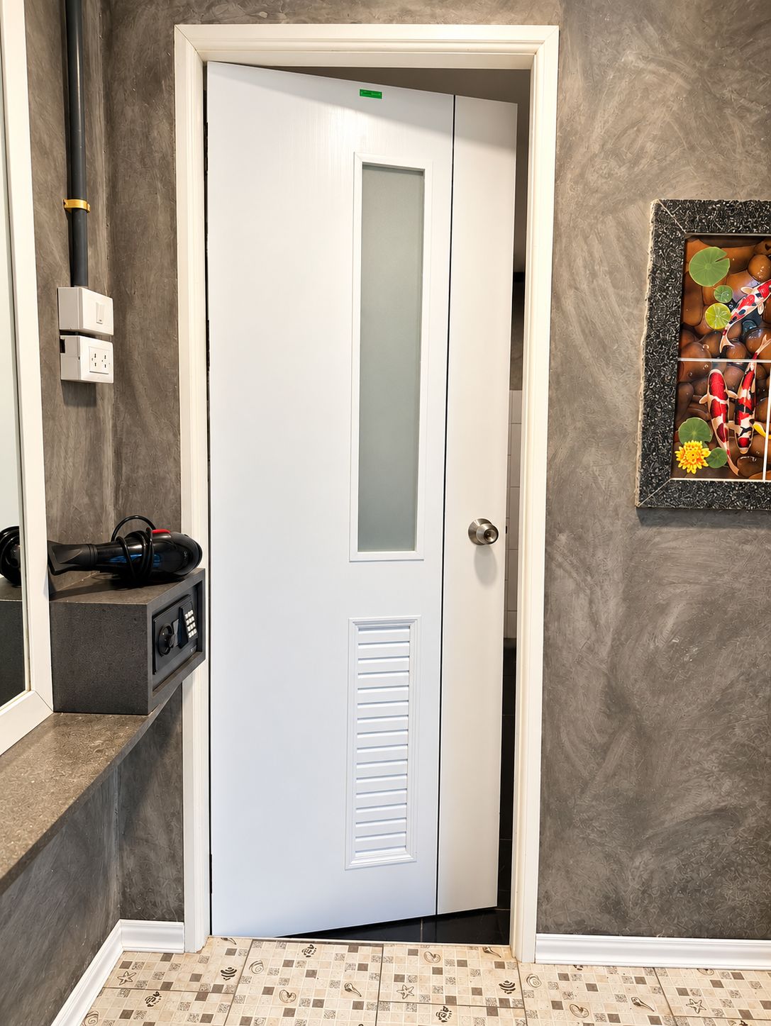 A white door with a frosted glass panel, a wall-mounted electrical outlet, and a framed picture of fish.
