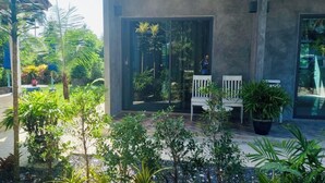 Un patio moderno al aire libre con dos sillas blancas, rodeado de abundante follaje y plantas en macetas.