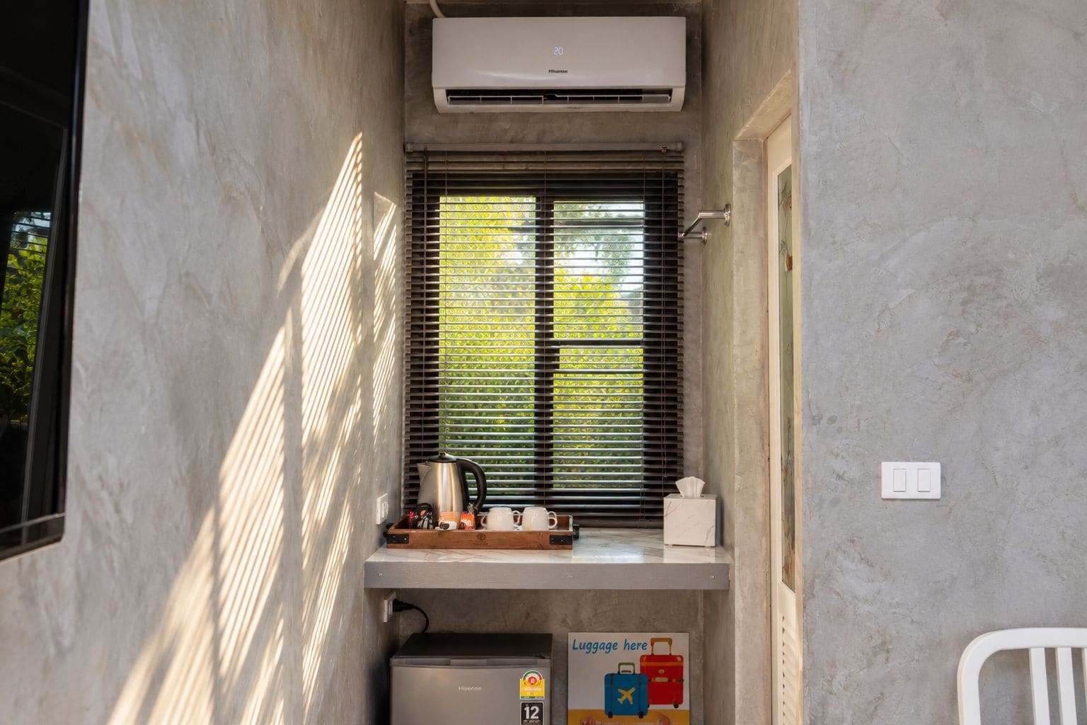 Une chambre de taille modeste, dotée d’une fenêtre, d’un petit coin cuisine et d’un espace pour entreposer les bagages.
