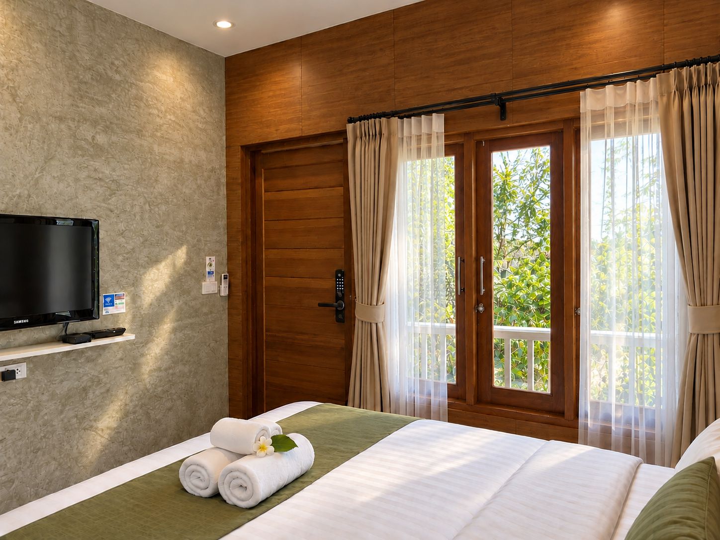 A hotel room with a bed, a television, a balcony with curtains, and a wooden door.