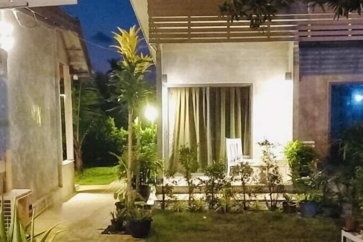 A modern house with a well-lit patio area, surrounded by potted plants and a small lawn.