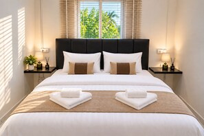 Een net opgemaakt bed met witte lakens, twee kussens en twee opgevouwen handdoeken op een beddekleed met een structuur in bruine tinten.