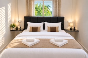 Una cama bien tendida con sábanas blancas, dos almohadas y dos toallas dobladas sobre un edredón marrón texturizado.