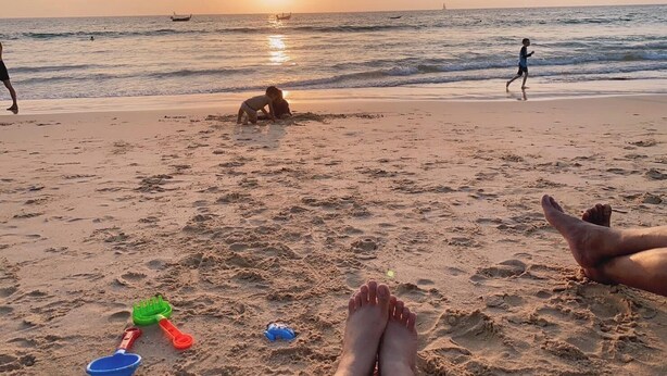 Escena de playa con huellas, un niño jugando y un atardecer.