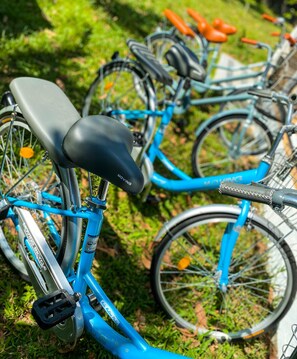 Ein blaues Fahrrad mit schwarzem Sattel und orangenen Griffen, abgestellt auf Rasen.