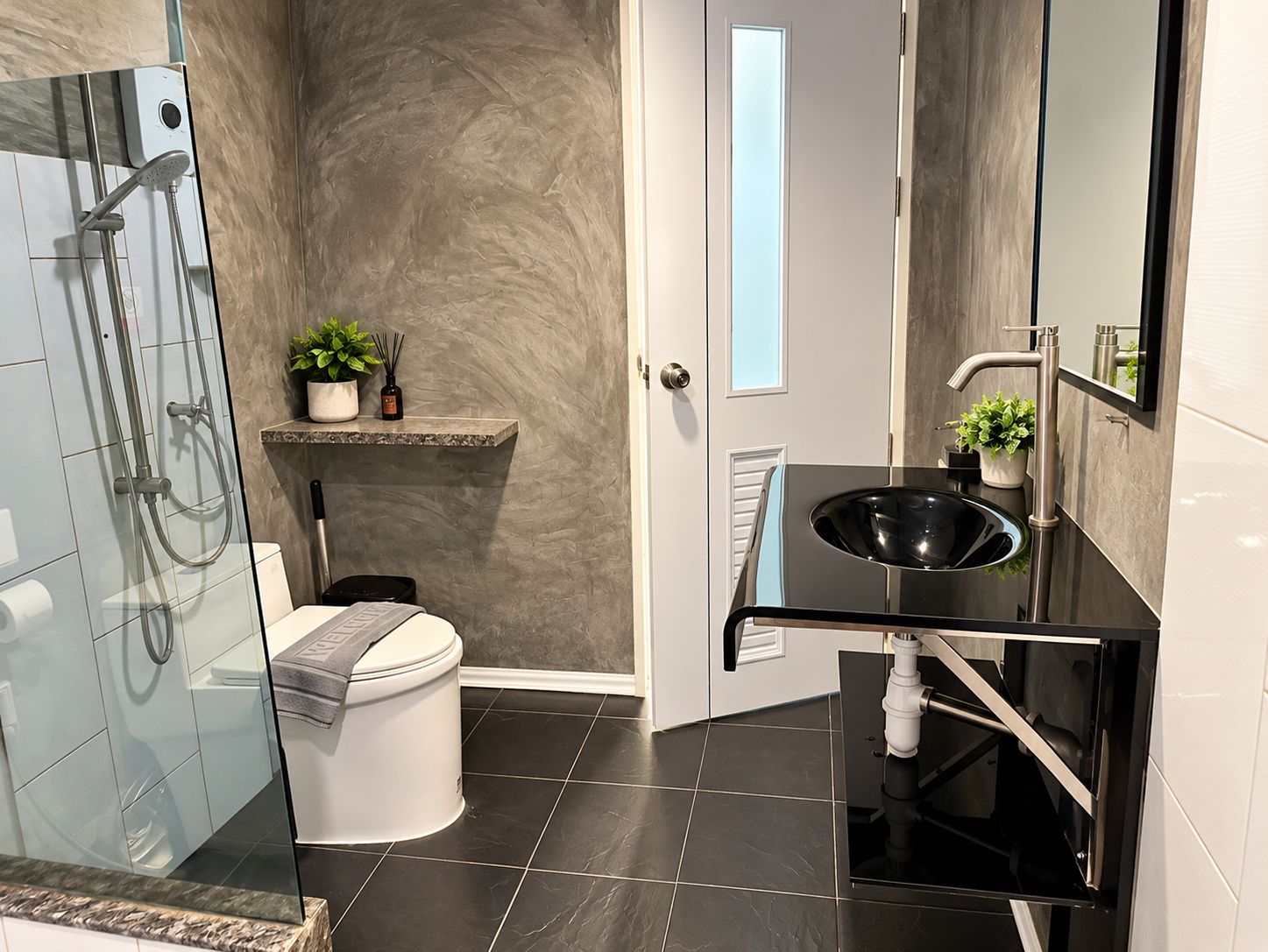 Une salle de bain moderne dotée d’une douche à parois de verre, de toilettes, d’un lavabo avec un plan de travail noir et d’un miroir au-dessus du lavabo.
