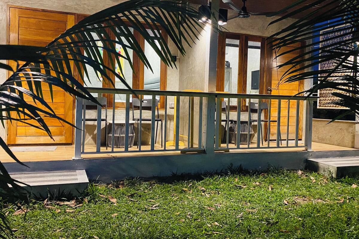 A covered outdoor seating area with a metal railing, a wooden door, and a ceiling fan.