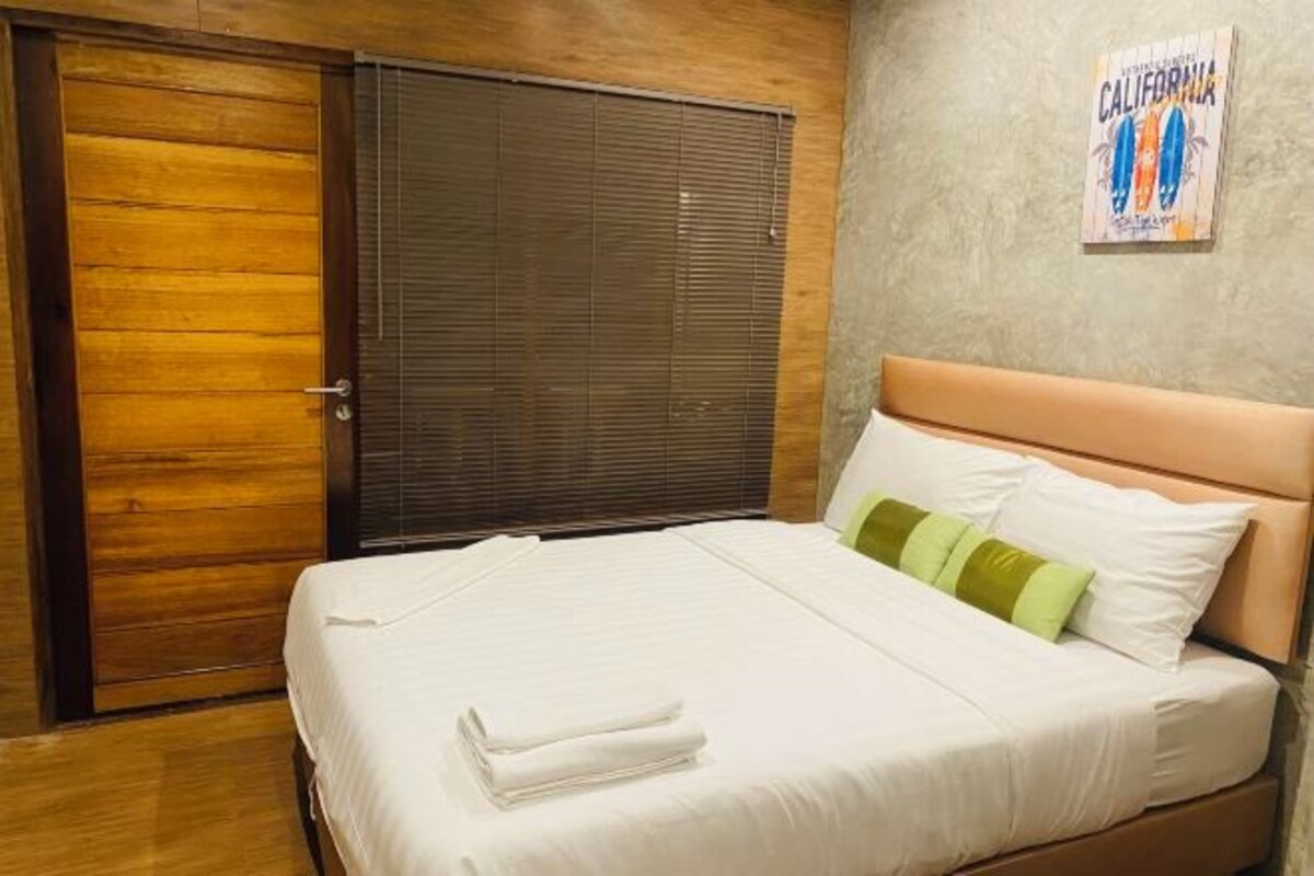 Habitación de hotel con una cama, una puerta de madera y una pared decorada con un póster de una tabla de surf californiana.
