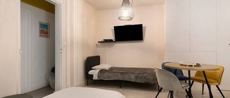 A bedroom with a bed, a desk, a chair, a television, and a dining table.