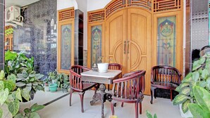 Una habitación con suelo de baldosas, una mesa de madera con dos sillas, una planta en maceta y un biombo decorativo de madera con diseños intrincados.