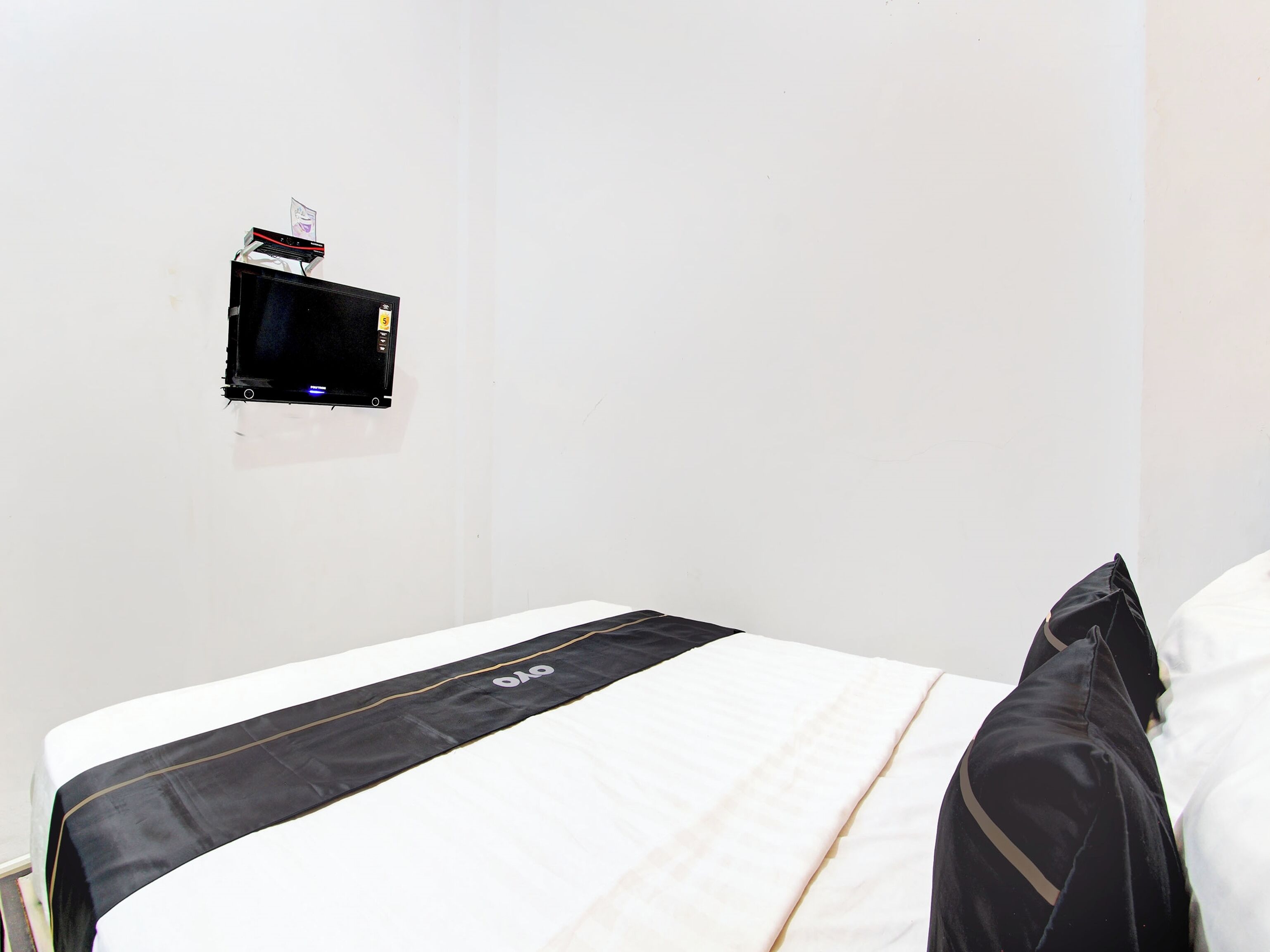A hotel room with a bed, a black and white striped bedspread, a black pillow, and a small black television mounted on the wall.