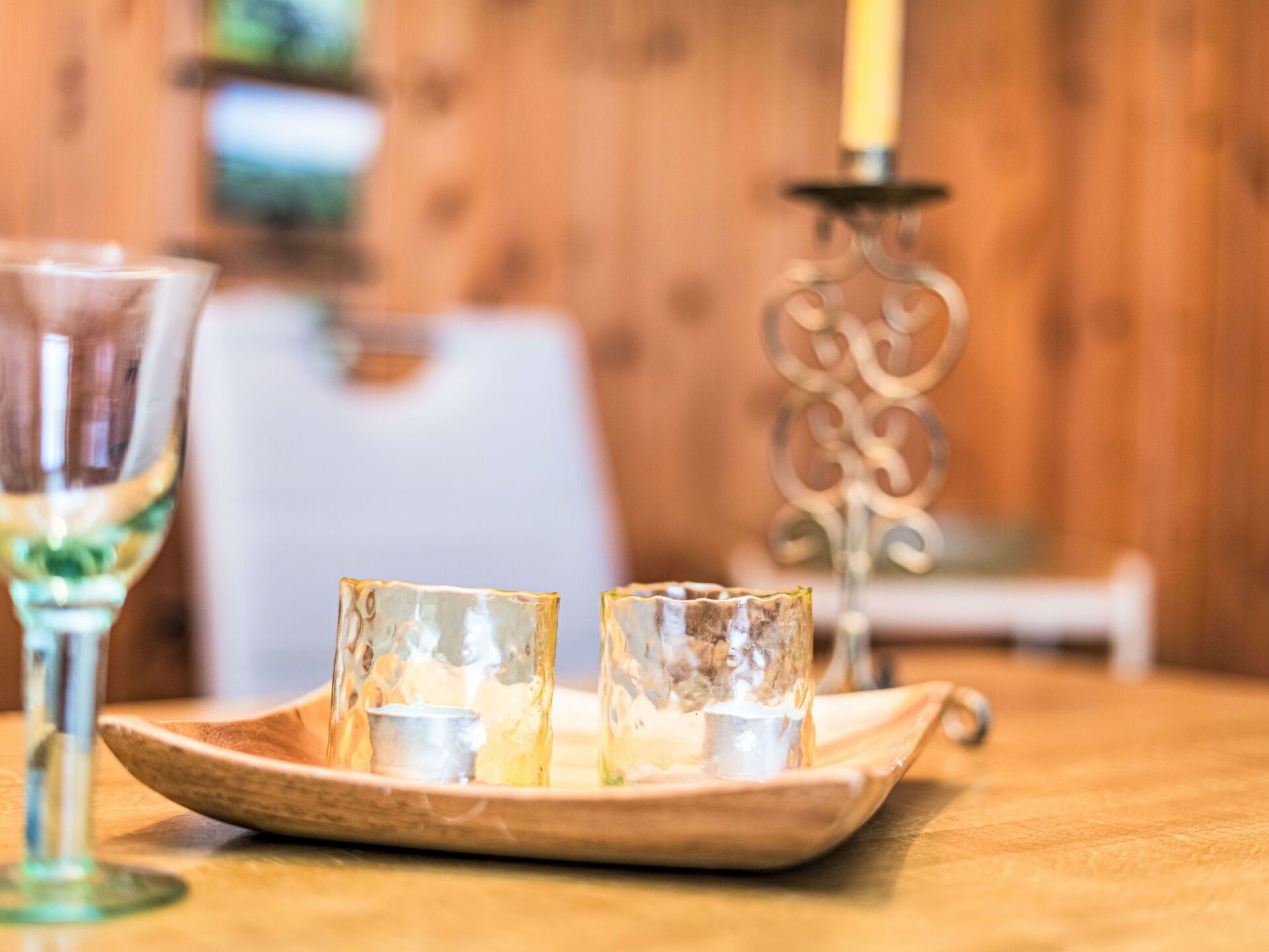 A wooden table with a tray holding three glasses of white wine, a candle holder, and a blurred background.