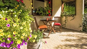 A patio area with a wooden table and chairs, surrounded by potted plants and flowers. - Lovely apartment for 2 people with WIFI, TV, patio and pets allowed (Bitburg)