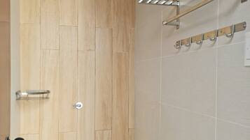 A bathroom with a wooden door, a shower with a rain showerhead, and a towel rack with hooks.